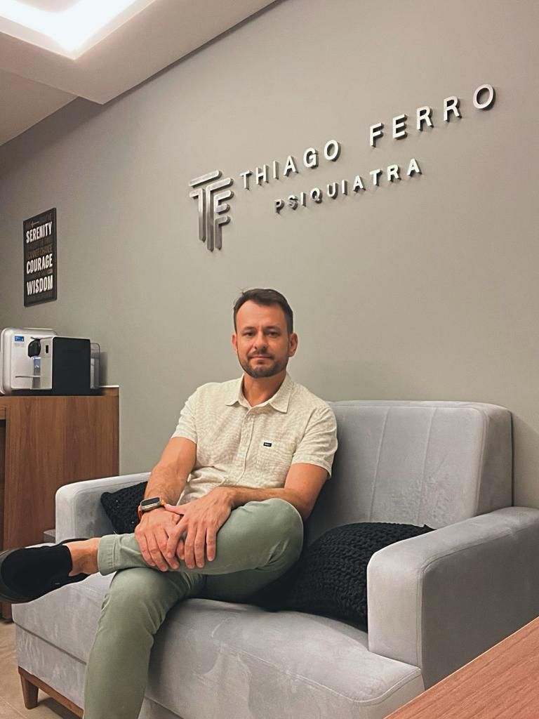Dr. Thiago Ferro em frente à identidade visual do consultório